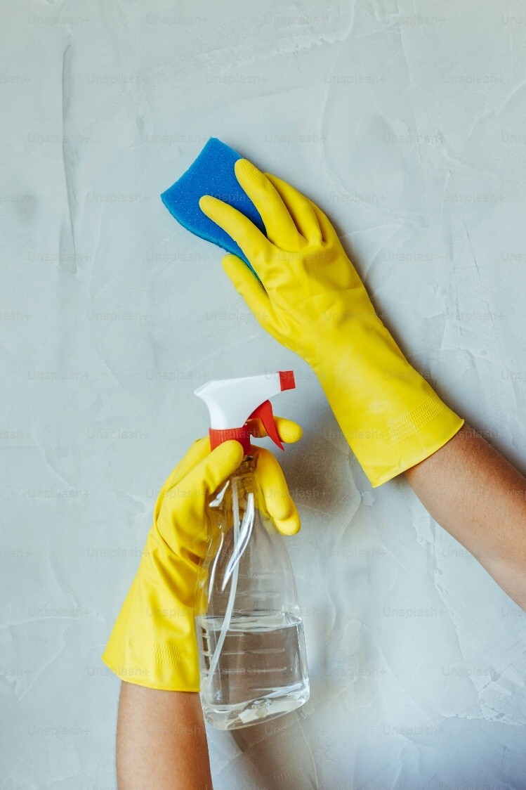 Hands in yellow rubber gloves cleaning a wall with a sponge