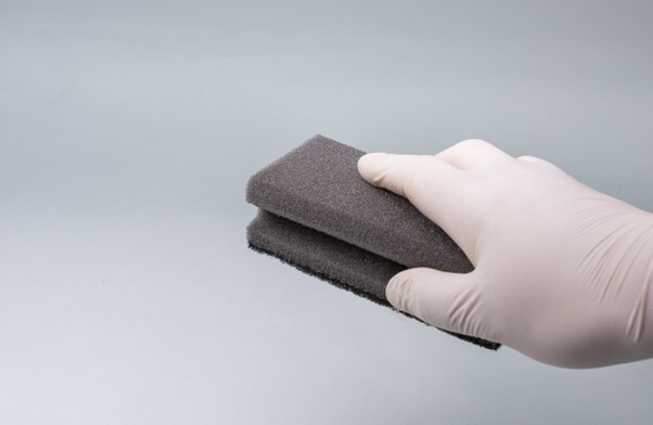 A hand wearing a glove and holding a sponge